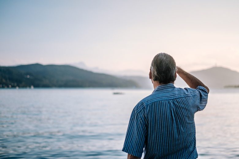 Older man in blue striped shirt stares out at ocean horizon